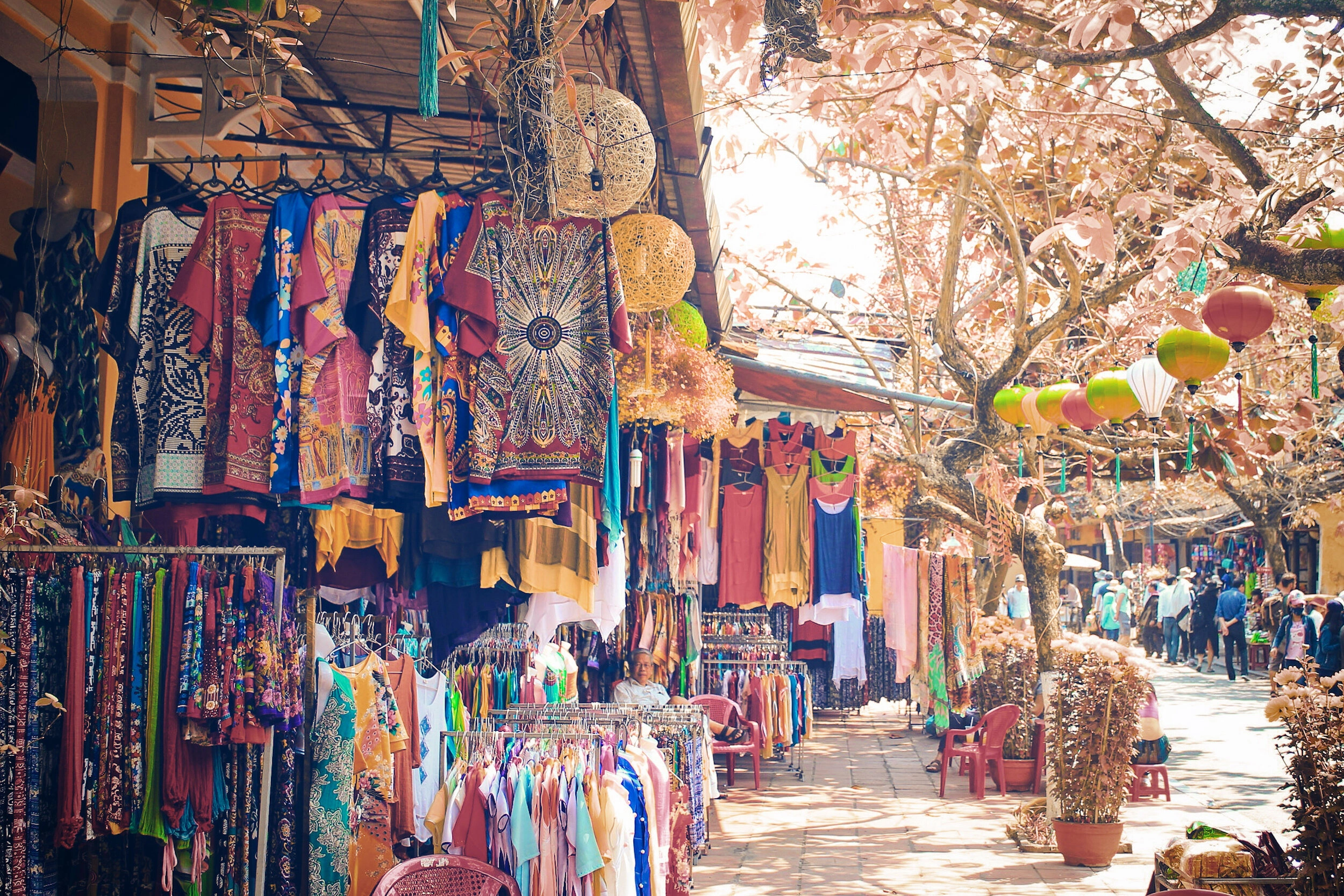 Colorful clothing stalls and hanging lanterns at Chatuchak Weekend Market in Bangkok, with shoppers exploring the vibrant outdoor market.